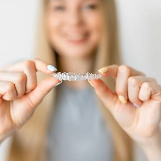 Smiling woman holding up Invisalign in Milton