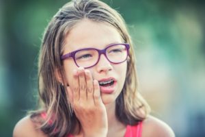 Child with braces holding her hand to her cheek from soreness