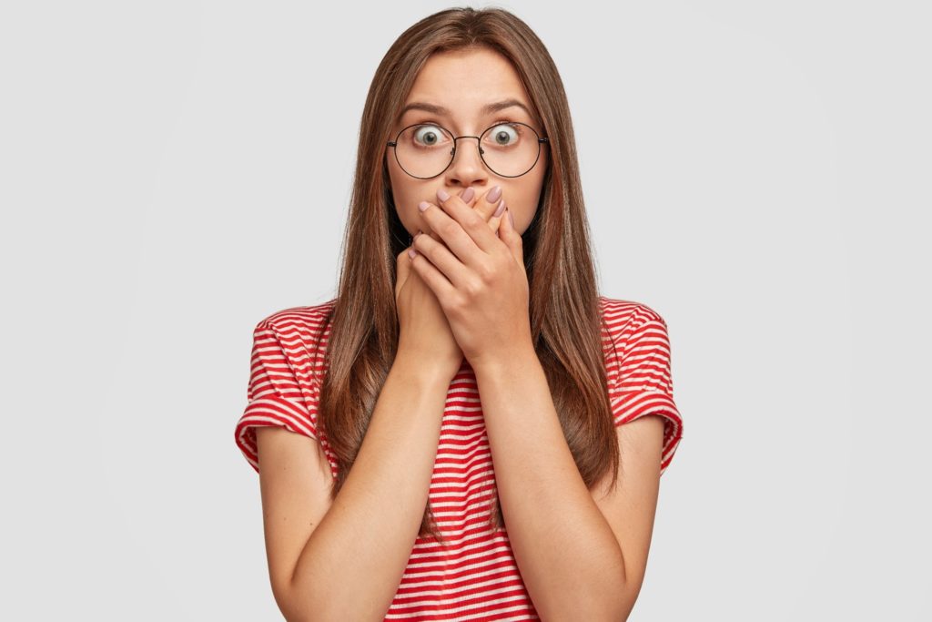 Girl with glasses covering her mouth in shock