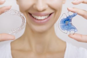 a patient smiling and holding her retainer