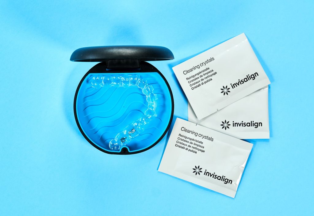 Invisalign aligners in tray next to packets of cleaning crystals